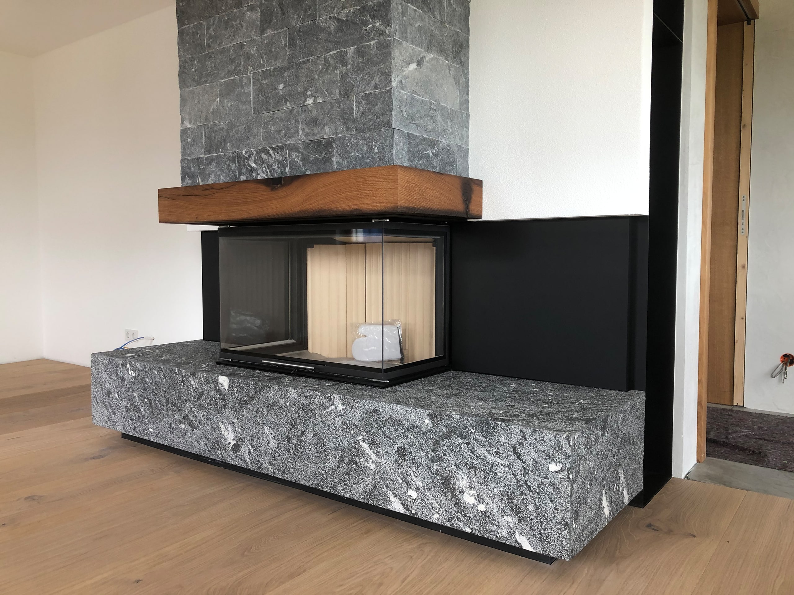 Eckkamin mit Sitzbank und Verblendung aus grauem Naturstein Rauriser dunkelblau und Holzsims