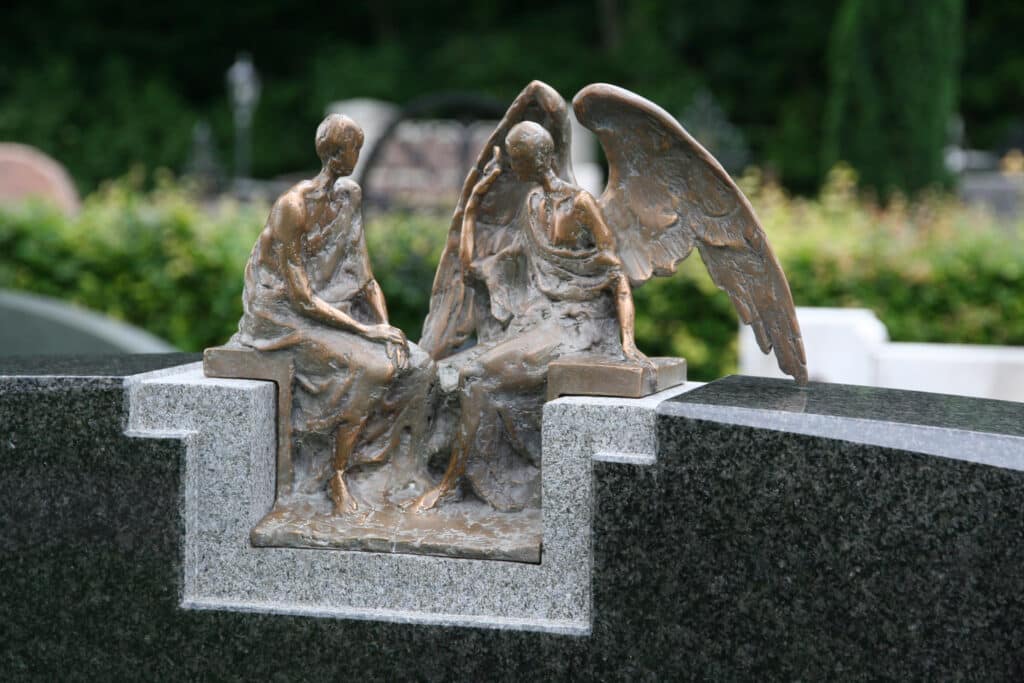 Bronzefigur eines Engels bei einer sitzenden Person auf einem Grabstein aus dunklem Granit