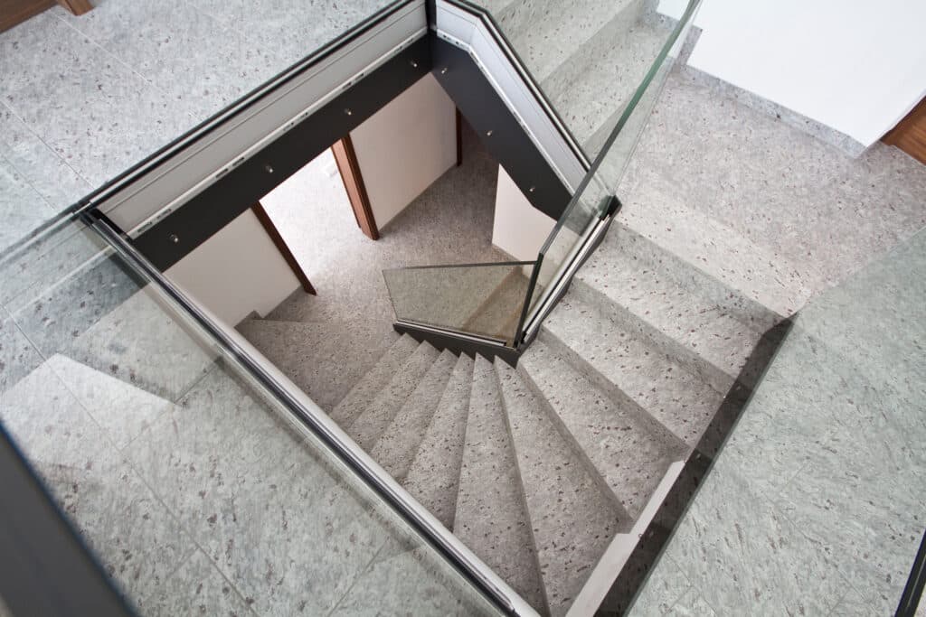 Blick von oben auf eine gewendelte Treppe aus Naturstein Blossom White mit Glasgeländer
