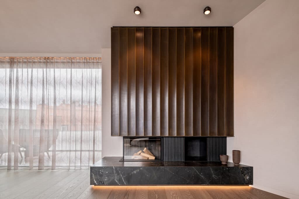 Kamin mit schwarz marmorierter Naturstein-Bank und geripptem Bronze-Aufsatz